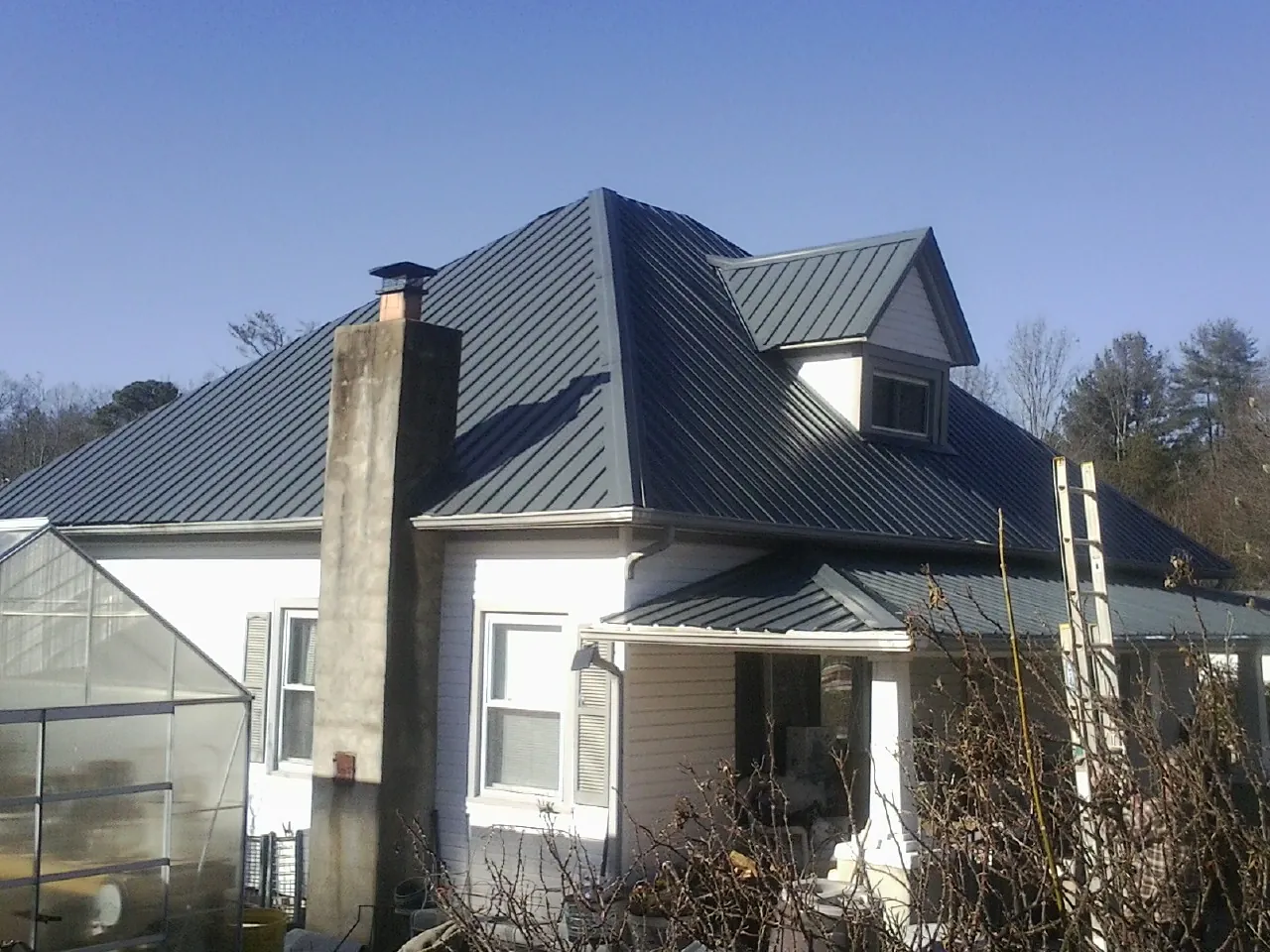 Dark blue standing seam metal roof on a white farmhouse with dormer — Slate & Tile Roof Repair by Roofing Brothers in Whitesville