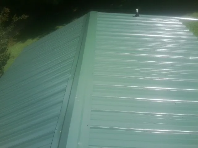 New green metal panels meeting at the ridge of a roof — Flat Roof Repair work by our crew in Whitesville