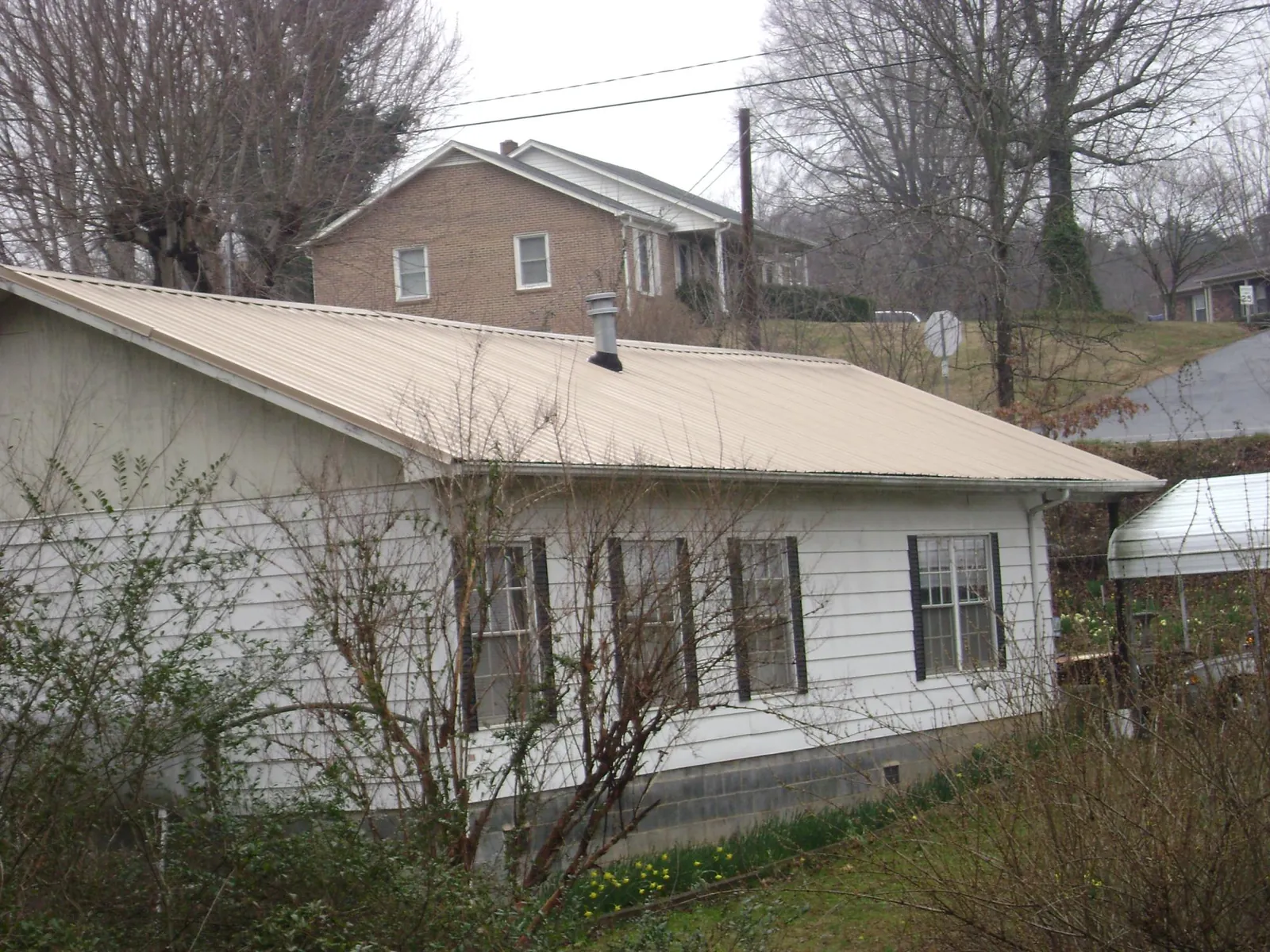 Tan metal roof on a white sided house set into a hillside — Commercial Roofing by Roofing Brothers in Whitesville